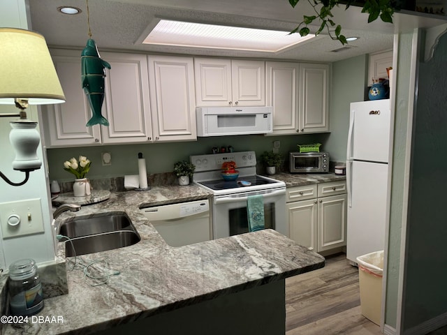 kitchen with sink, kitchen peninsula, white appliances, light hardwood / wood-style flooring, and white cabinets