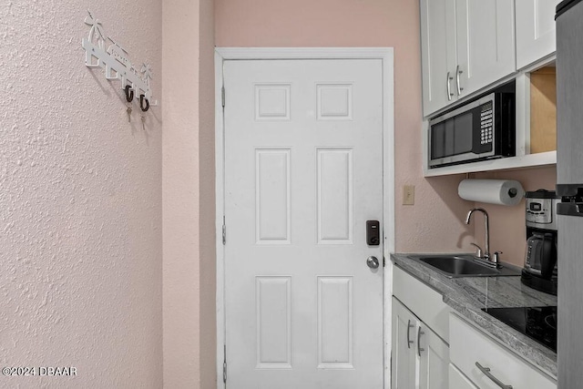 kitchen with black appliances, light stone counters, white cabinets, and sink