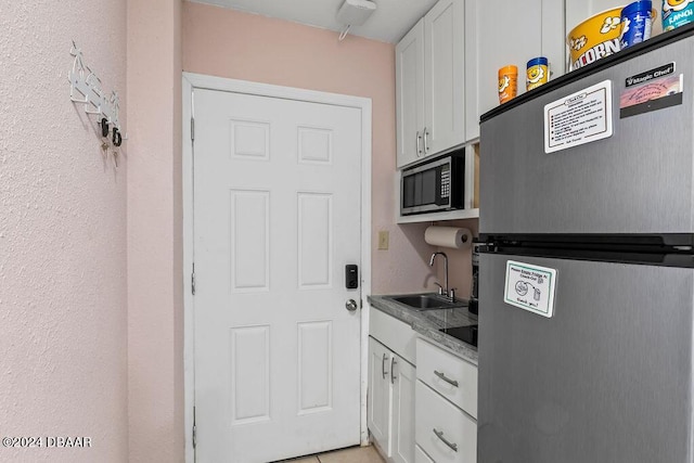 kitchen with stainless steel refrigerator, white cabinetry, built in microwave, sink, and light tile patterned floors