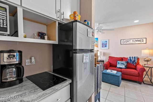 kitchen with white cabinets, ceiling fan, black electric cooktop, light tile patterned flooring, and stainless steel refrigerator