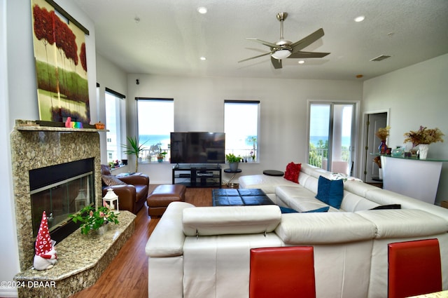 living room featuring a textured ceiling, ceiling fan, a fireplace, and dark hardwood / wood-style floors