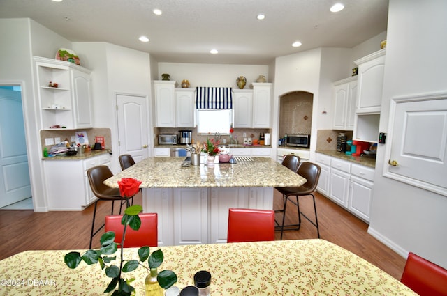 kitchen with a breakfast bar area, white cabinetry, a center island, and hardwood / wood-style floors