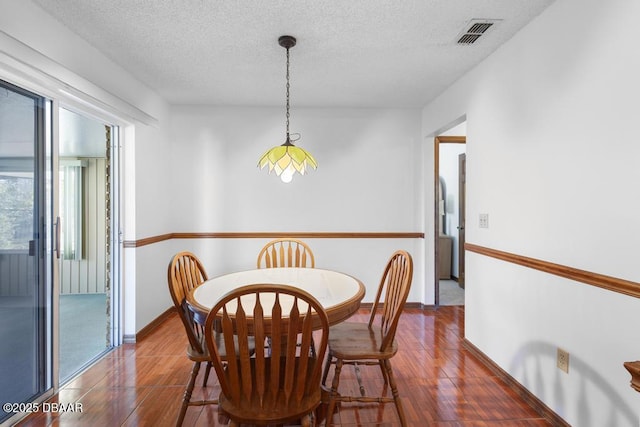 dining area with baseboards, a textured ceiling, visible vents, and wood finished floors