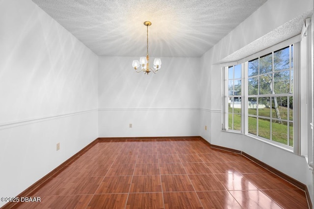 empty room with a chandelier, a textured ceiling, and baseboards