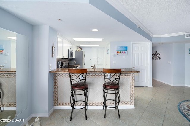 kitchen featuring light tile patterned floors, a kitchen bar, stainless steel appliances, and a peninsula
