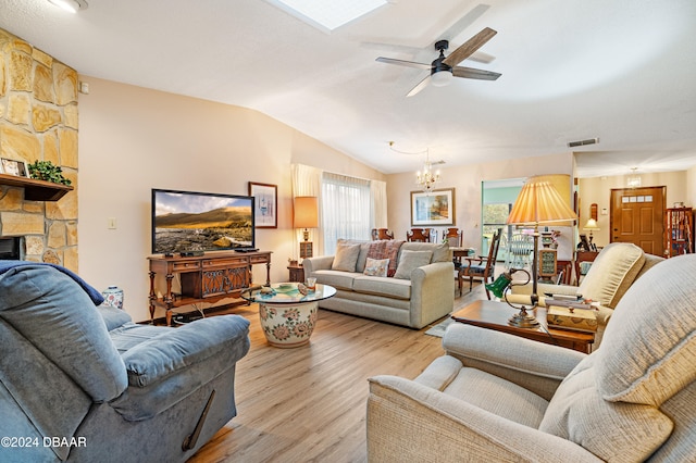 living room with ceiling fan with notable chandelier, light hardwood / wood-style floors, a fireplace, and vaulted ceiling