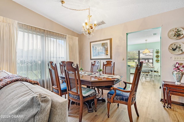 dining room with light wood-type flooring, an inviting chandelier, vaulted ceiling, and a wealth of natural light