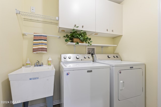 clothes washing area with separate washer and dryer, sink, and cabinets