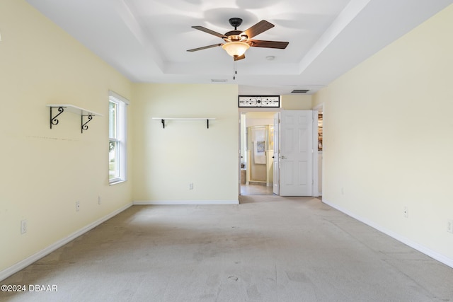 carpeted empty room featuring ceiling fan and a raised ceiling