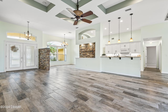 unfurnished living room with french doors, a towering ceiling, coffered ceiling, ceiling fan with notable chandelier, and wood-type flooring