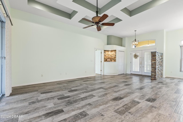 unfurnished living room with coffered ceiling, french doors, ceiling fan with notable chandelier, and hardwood / wood-style flooring