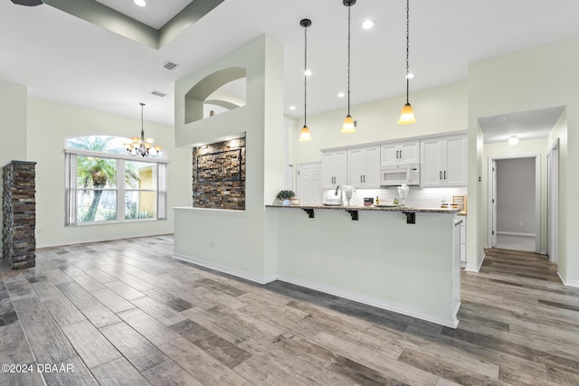 kitchen with kitchen peninsula, hardwood / wood-style floors, white cabinetry, and a kitchen breakfast bar