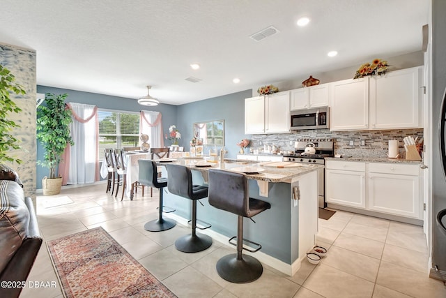 316 Nowell Loop, Deland, FL 32724 - kitchen featuring stainless steel appliances, white cabinetry, backsplash, light stone counters, and a kitchen breakfast bar