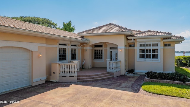 property entrance featuring driveway, a tiled roof, covered porch, stucco siding, and a garage