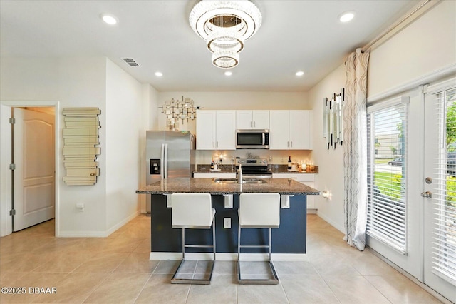 3049 Meleto Blvd, New Smyrna Beach, FL 32168 - kitchen with stainless steel appliances, a center island with sink, white cabinets, a kitchen breakfast bar, and dark stone counters
