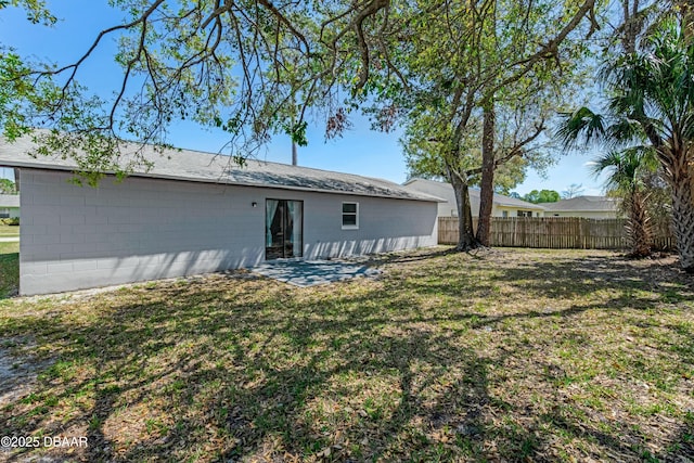 back of property with concrete block siding, a yard, and fence