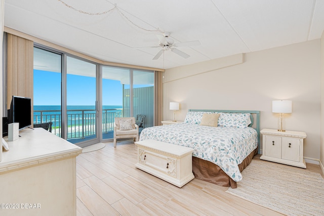 bedroom with floor to ceiling windows, ceiling fan, access to outside, a water view, and hardwood / wood-style flooring