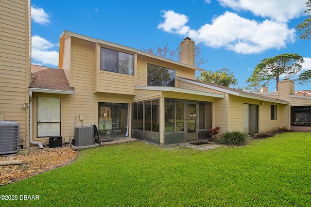 back of property with a sunroom, a lawn, and central AC