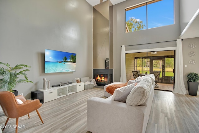 living room with a high ceiling, a wealth of natural light, light hardwood / wood-style flooring, and a fireplace