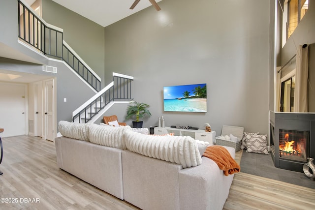 living room featuring light hardwood / wood-style floors, ceiling fan, and a towering ceiling