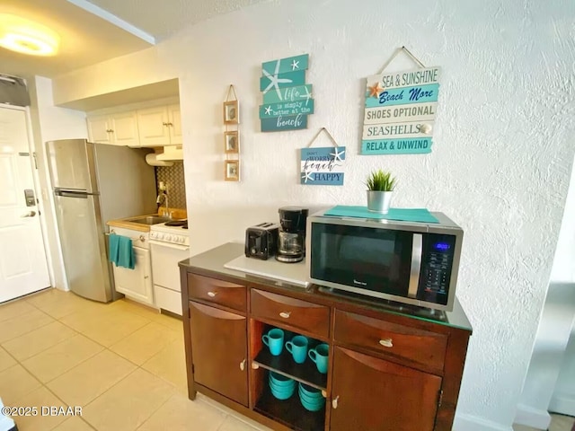 3501 S Atlantic Ave Unit 622, Daytona Beach, FL 32118 - kitchen featuring appliances with stainless steel finishes, light tile patterned floors, a textured wall, under cabinet range hood, and white cabinets