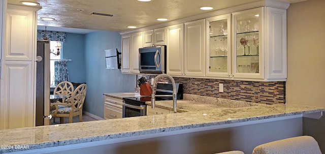 kitchen with white cabinets, hanging light fixtures, backsplash, and appliances with stainless steel finishes