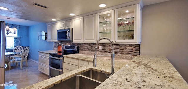 kitchen with backsplash, appliances with stainless steel finishes, hanging light fixtures, white cabinets, and a chandelier