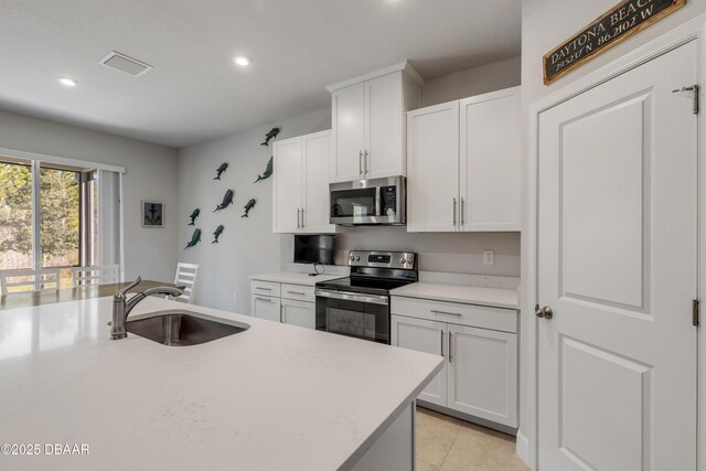 kitchen with an island with sink, light tile patterned floors, white cabinetry, appliances with stainless steel finishes, and sink