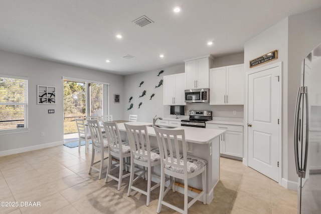 kitchen with stainless steel appliances, white cabinets, a kitchen bar, light tile patterned floors, and a center island with sink