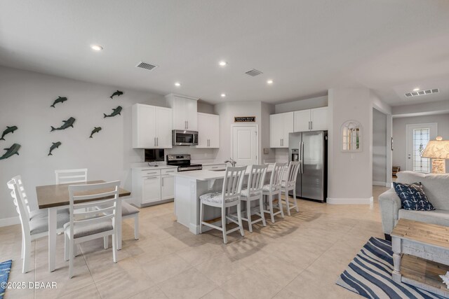 kitchen with light tile patterned floors, a kitchen bar, a kitchen island with sink, white cabinetry, and appliances with stainless steel finishes