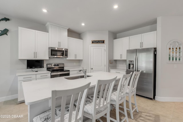 kitchen featuring stainless steel appliances, an island with sink, white cabinetry, light tile patterned flooring, and sink