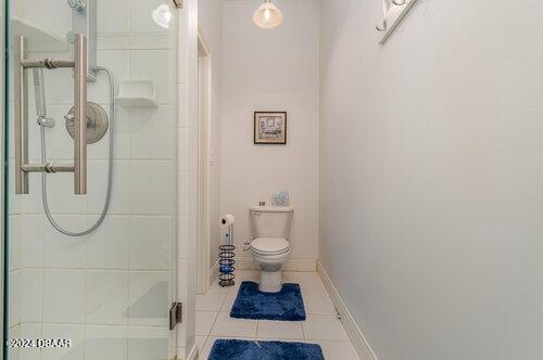 bathroom featuring toilet, a shower stall, tile patterned flooring, and baseboards