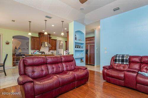 living area with arched walkways, light wood finished floors, built in shelves, and visible vents