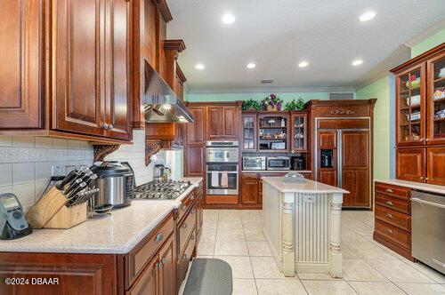 kitchen with light tile patterned floors, ornamental molding, ventilation hood, light countertops, and stainless steel appliances