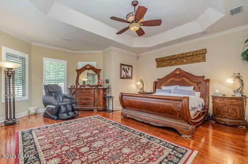 bedroom featuring visible vents, baseboards, crown molding, a tray ceiling, and wood finished floors