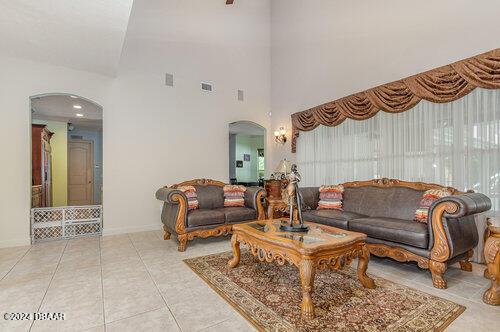 tiled living area featuring visible vents, baseboards, arched walkways, and a high ceiling