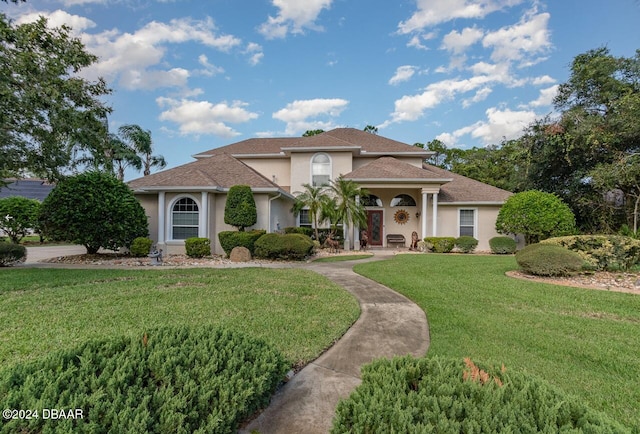 mediterranean / spanish home featuring a shingled roof, stucco siding, and a front lawn