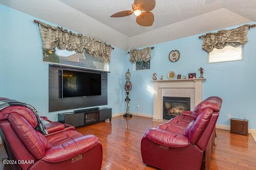 living room featuring a ceiling fan, a glass covered fireplace, vaulted ceiling, wood finished floors, and baseboards