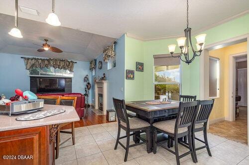 dining room with a fireplace, light tile patterned floors, ceiling fan with notable chandelier, and baseboards