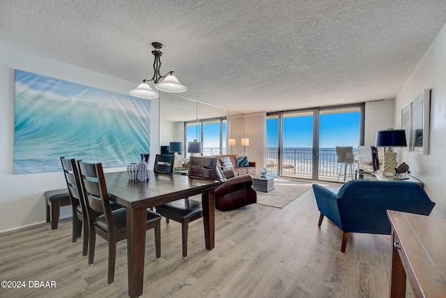 dining space featuring a water view, a textured ceiling, floor to ceiling windows, and light hardwood / wood-style flooring