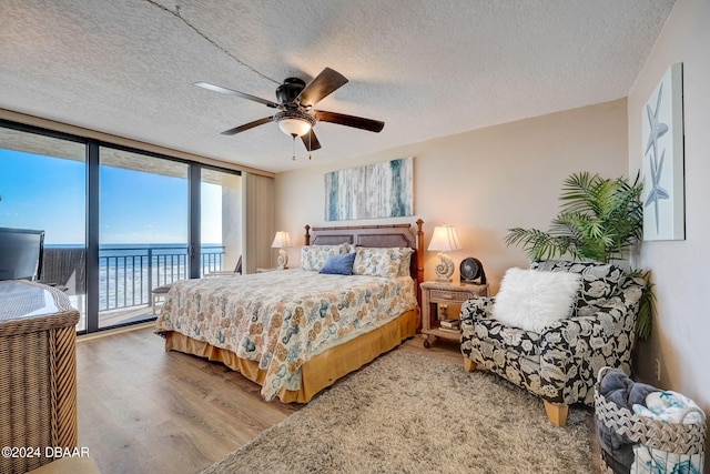 bedroom featuring ceiling fan, a textured ceiling, access to exterior, a wall of windows, and hardwood / wood-style floors