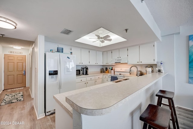 kitchen with light hardwood / wood-style floors, extractor fan, kitchen peninsula, a kitchen breakfast bar, and white appliances