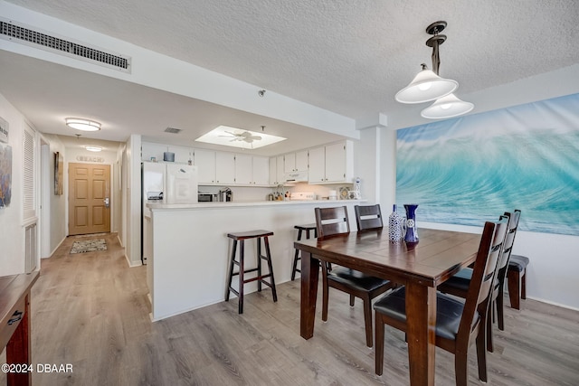 dining space with a skylight, a textured ceiling, and light hardwood / wood-style floors