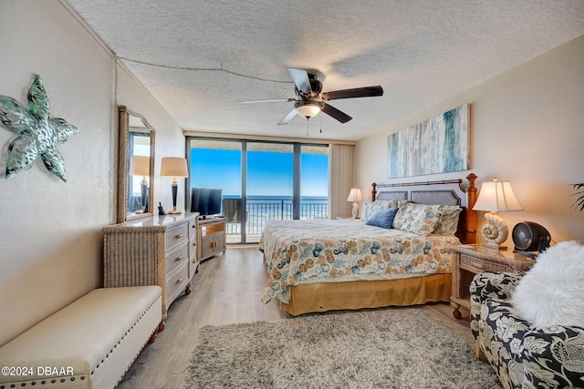 bedroom with access to outside, a textured ceiling, expansive windows, hardwood / wood-style flooring, and ceiling fan