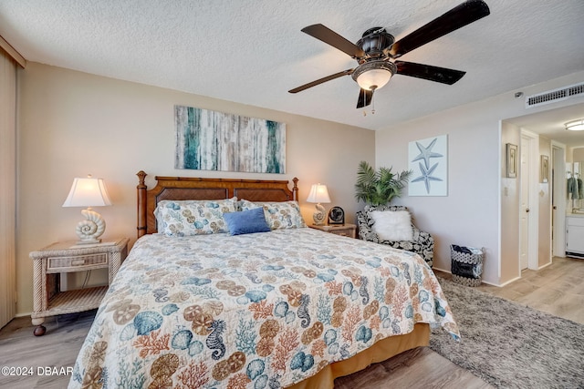 bedroom with a textured ceiling, light hardwood / wood-style floors, and ceiling fan