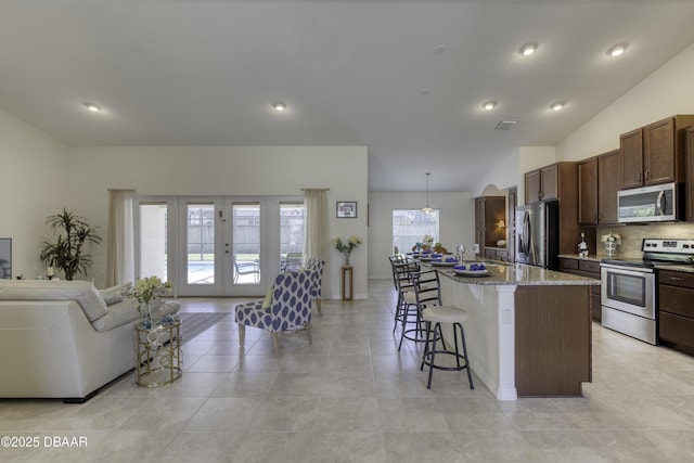 kitchen featuring a kitchen bar, visible vents, a center island with sink, open floor plan, and appliances with stainless steel finishes