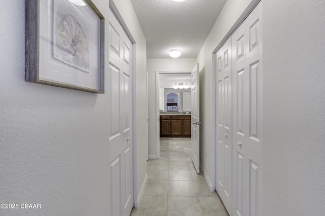 hall with light tile patterned floors, baseboards, a textured ceiling, and a textured wall