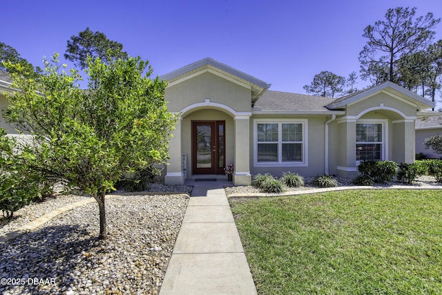 ranch-style home with stucco siding, a front yard, and roof with shingles