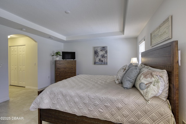 bedroom featuring visible vents, a raised ceiling, arched walkways, light tile patterned floors, and baseboards