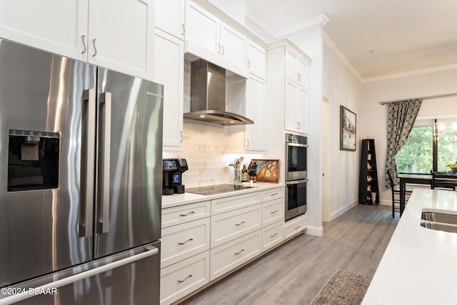 kitchen with appliances with stainless steel finishes, light wood-type flooring, wall chimney exhaust hood, crown molding, and white cabinets